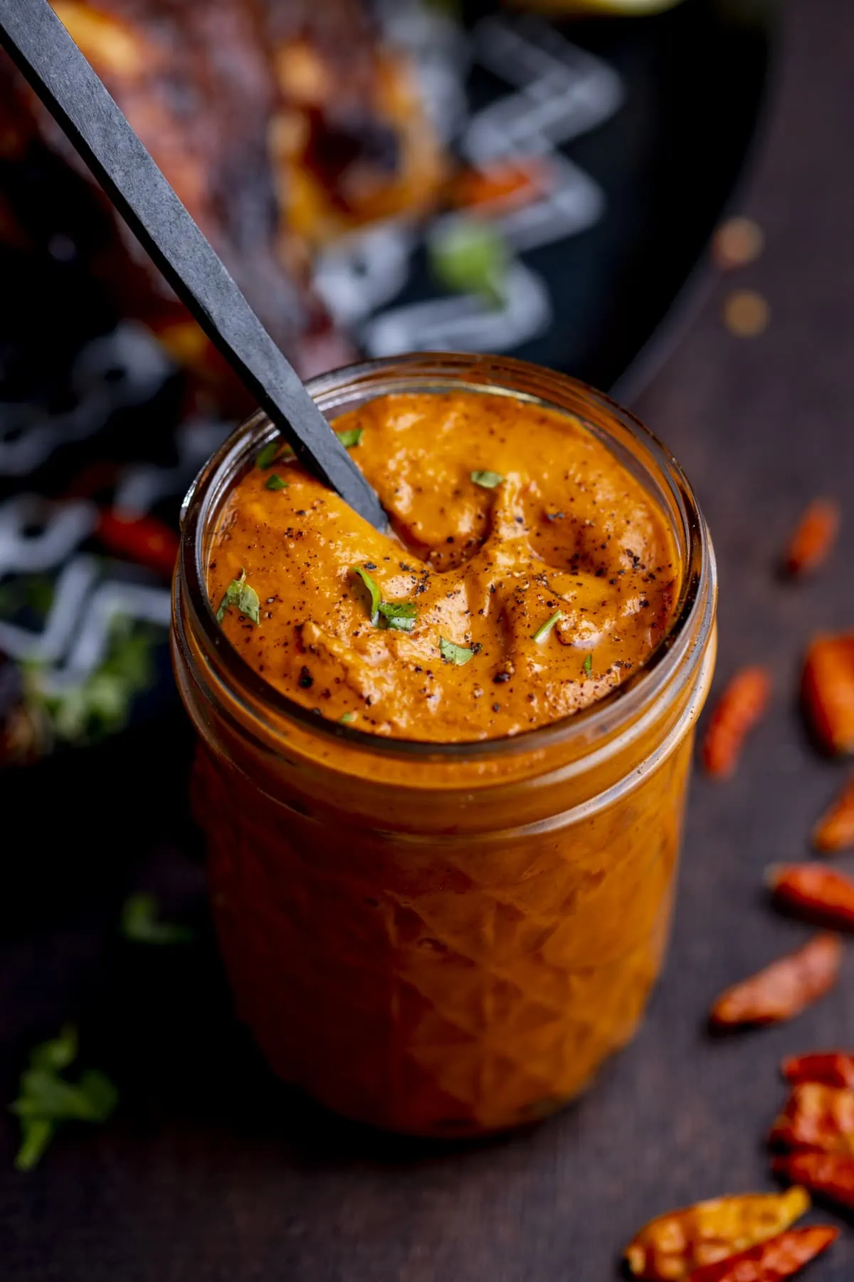 Homemade peri peri sauce in a glass jar with a black spoon sticking out of it.