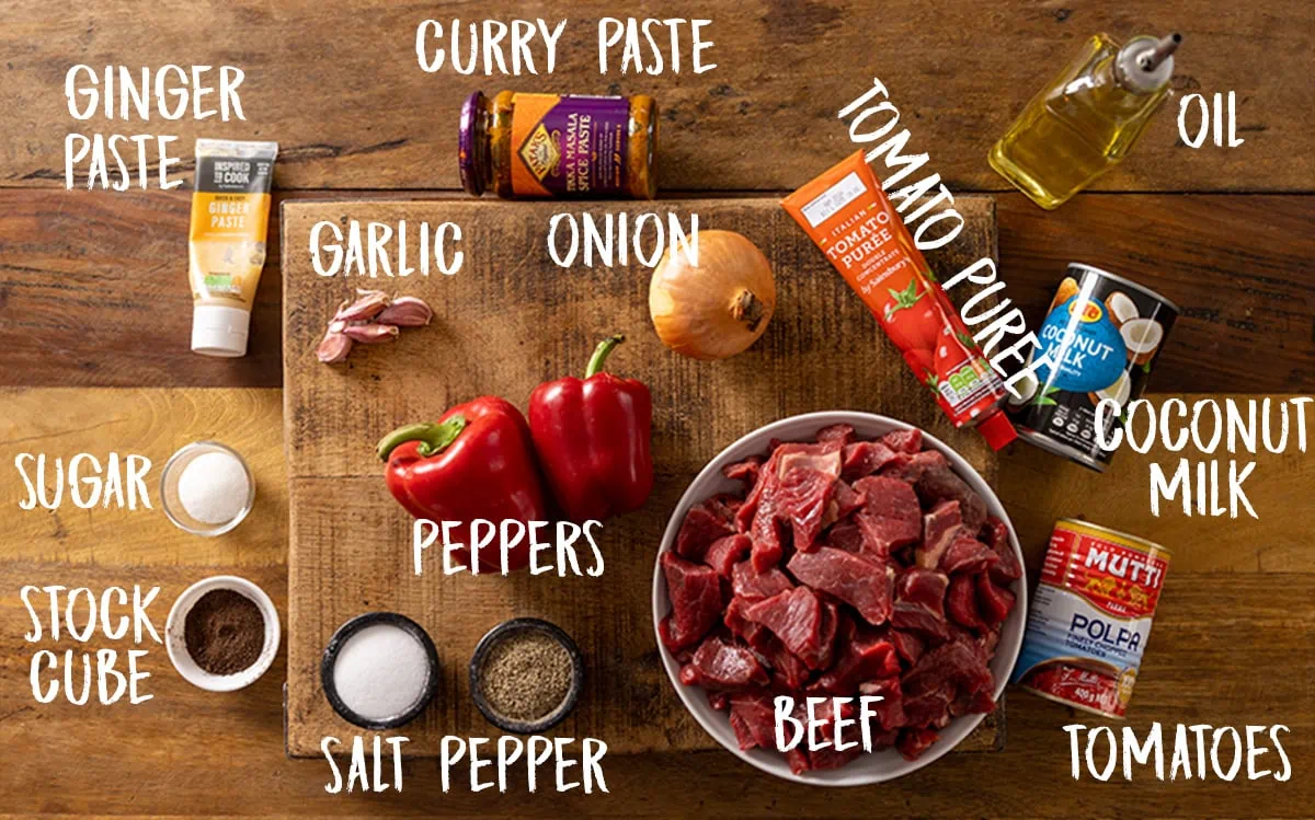 Ingredients for a slow cooker coconut beef curry on a wooden table.