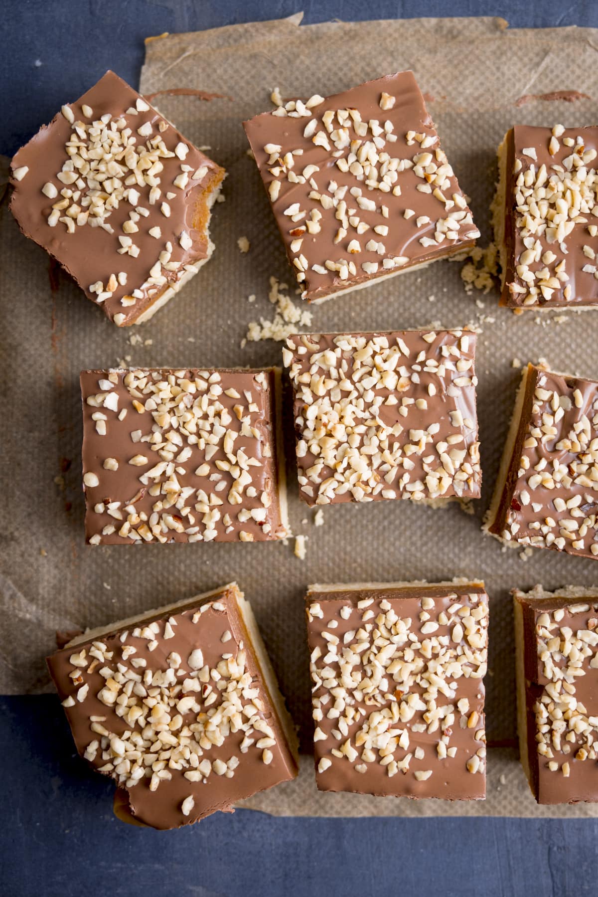 Overhead image of squares of millionaire's shortbread, top with chopped hazelnuts, on a piece of parchment paper. There is a bite taken out of one of the squares.