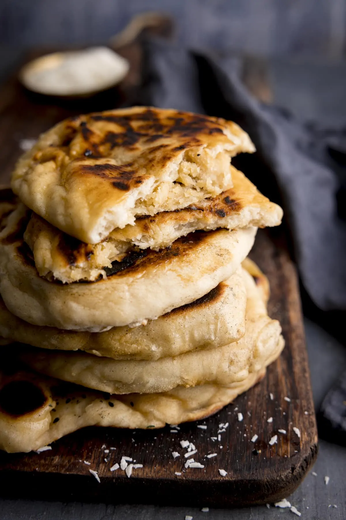A stack of peshwari naan breads on a dark wooden board against a blue background. There is a blue napkin in shot. The top naan has been broken into two to show the filling.