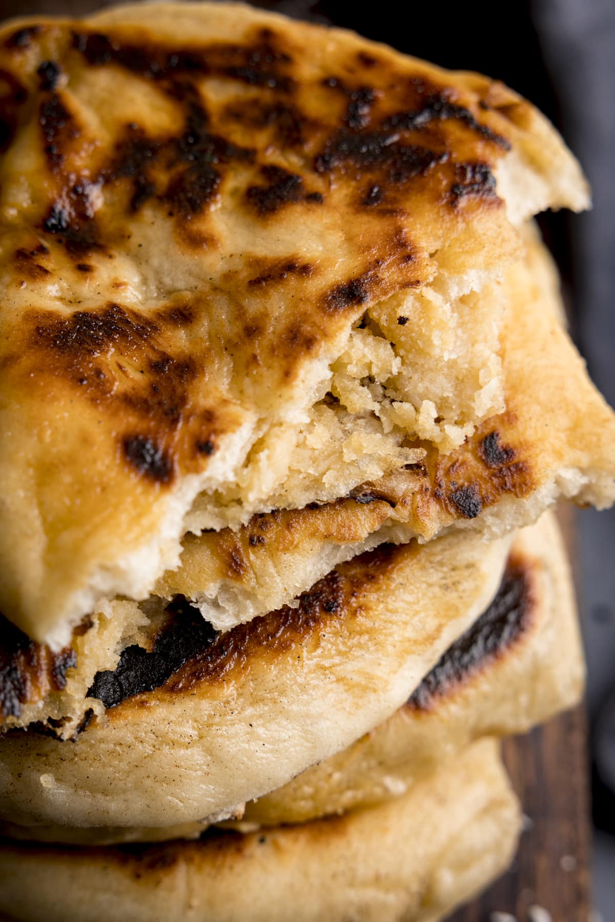 Close up overhead image of a stack of peshwari naan breads on a wooden board. The top naan has been torn in two, to reveal the filling.
