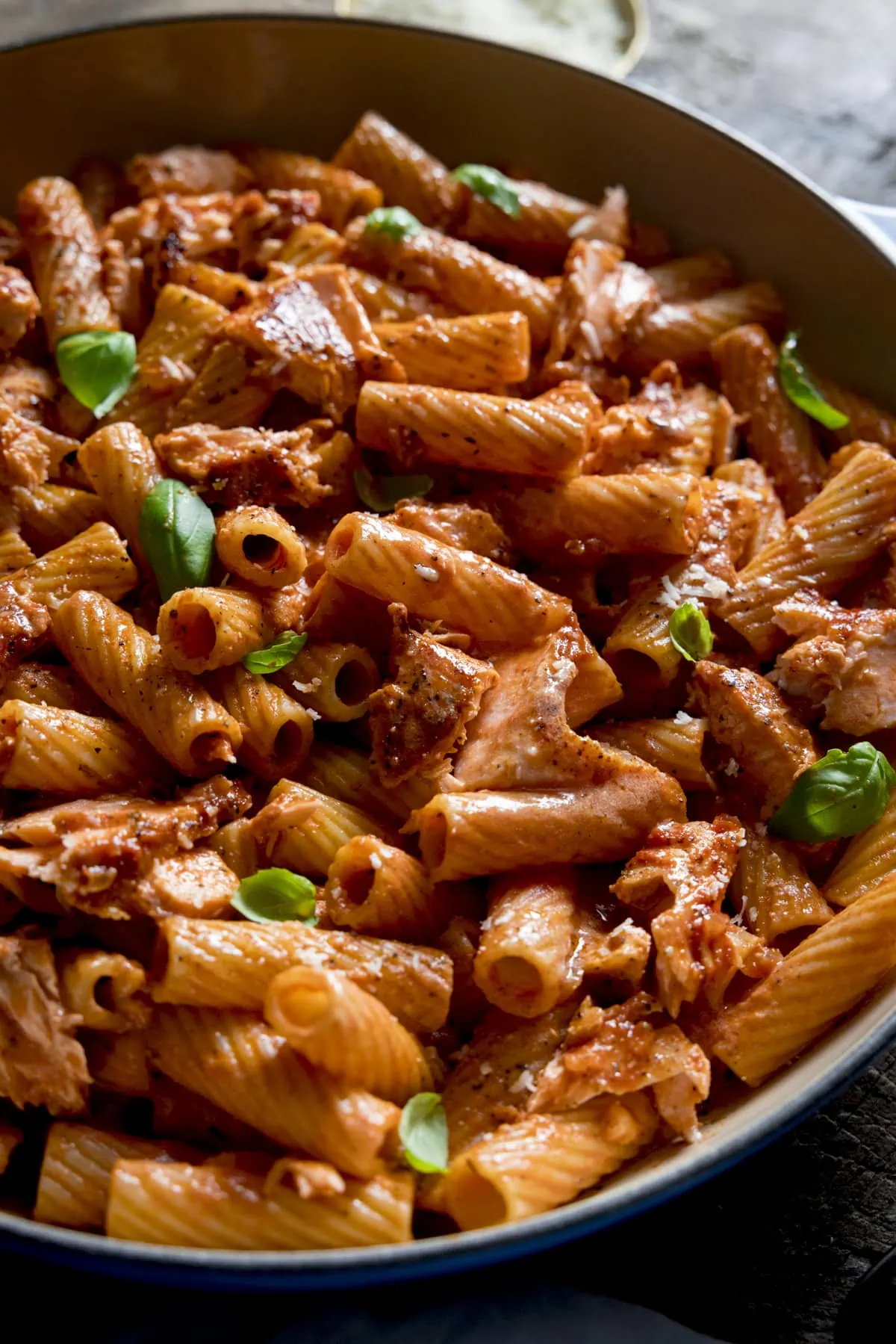 Close up of creamy tomato salmon rigatoni in a pan, topped with a sprinkling of basil leaves.