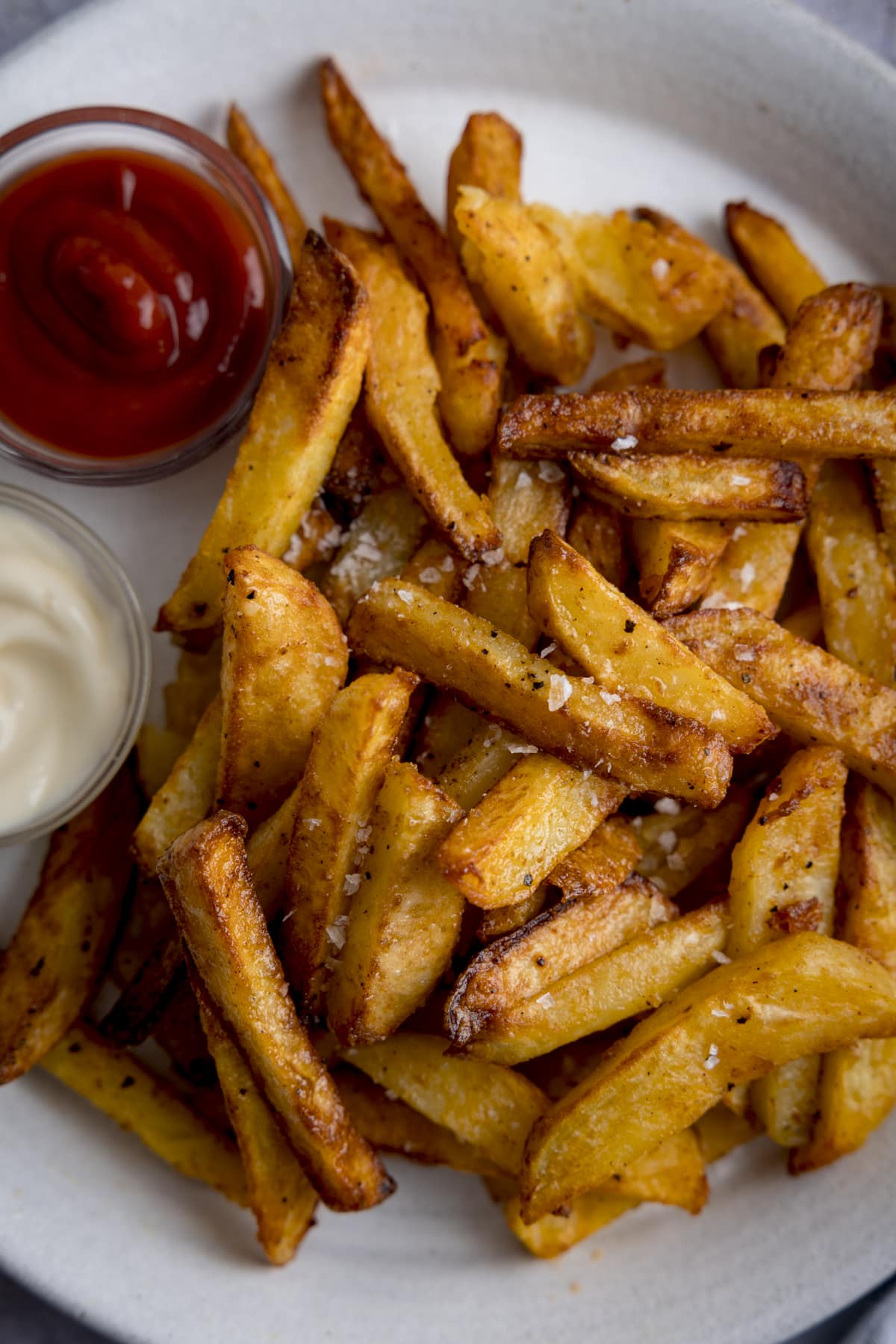 A tall overhead shot of air chips on a white plate next to two small dipping bowls - one filled with ketchup, one filled with mayonnaise