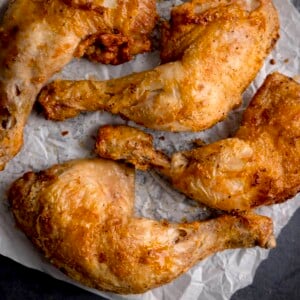 Square image of four air fried crispy chicken legs on a piece of baking parchment.