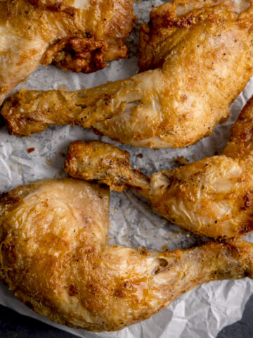 Square image of four air fried crispy chicken legs on a piece of baking parchment.
