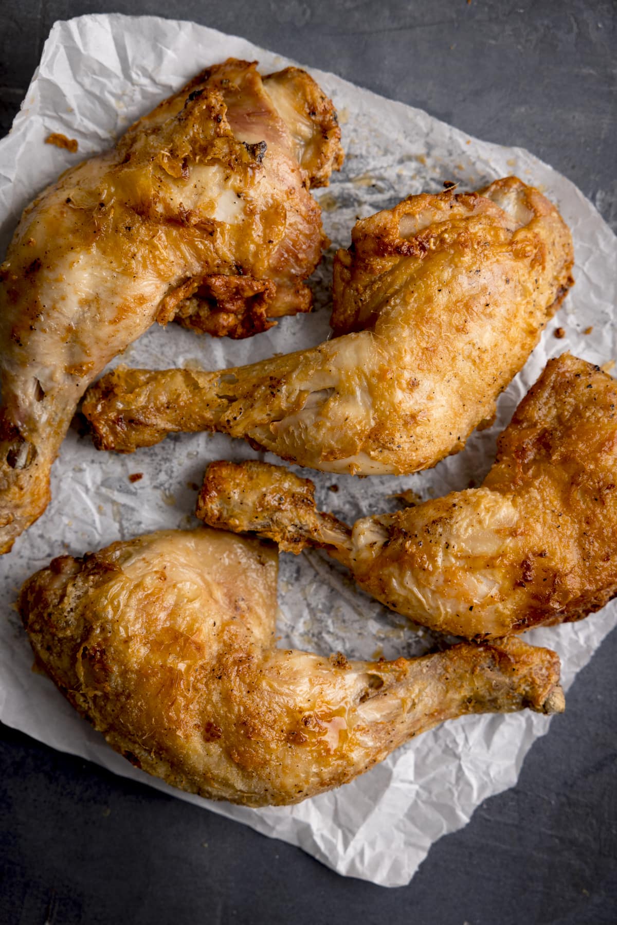 Large overhead image of four air fried, crispy chicken thighs on a piece of parchment paper.