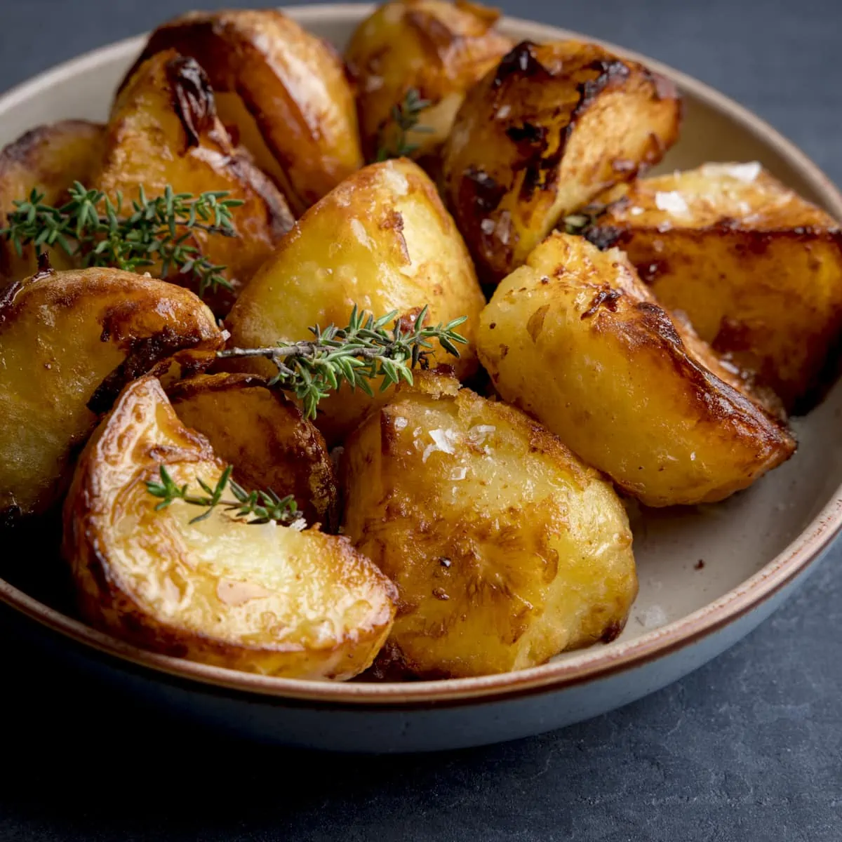 Square image of a bowl filled with Air Fryer Roast Potatoes, sprinkled with salt and parsley, on a dark blue background.