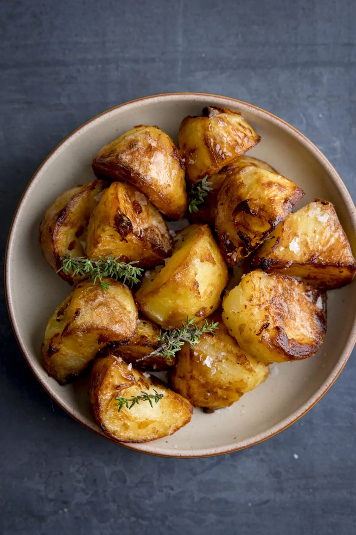 An overhead image of a bowl filled with Air Fryer Roast Potatoes, all crispy and golden and sprinkled with parsley and salt, on a dark blue background.