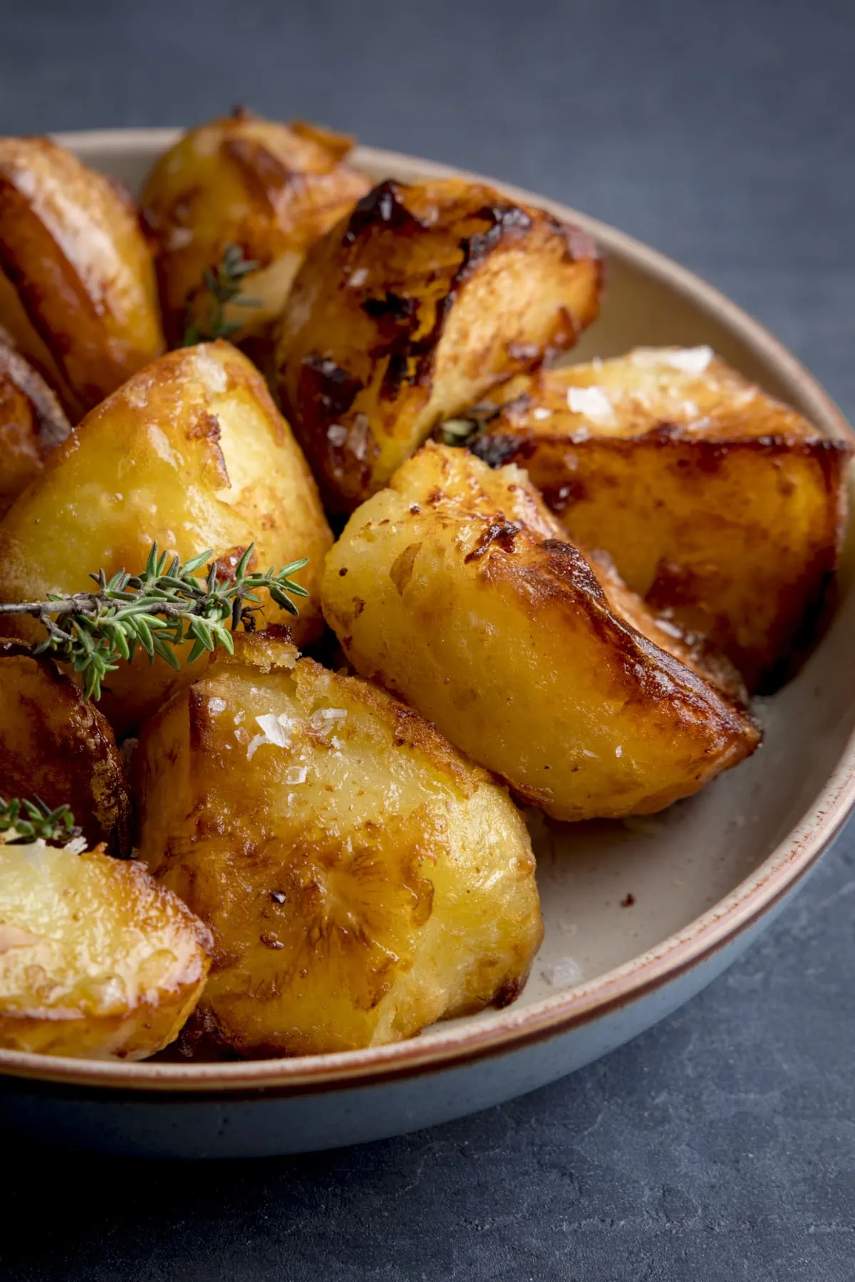 Close up shot of a bowl filled with Air Fryer Roast Potatoes, sprinkled with parsley and salt, on a dark blue background.