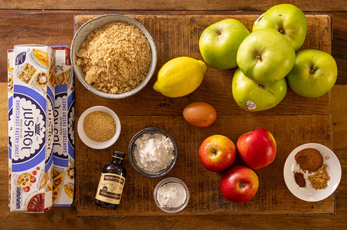 Ingredients for apple pie laid out on a wooden board.