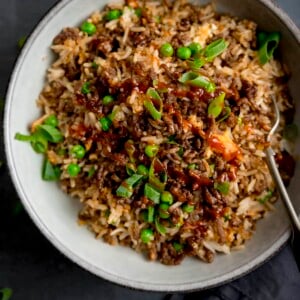 Square image of a bowl of minced beef fried rice, topped with sliced spring onions. There is a fork sticking out of the bowl.