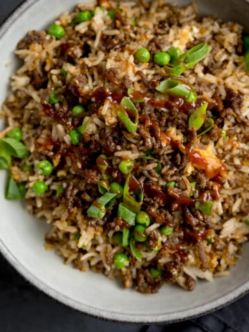 Square image of a bowl of minced beef fried rice, topped with sliced spring onions. There is a fork sticking out of the bowl.