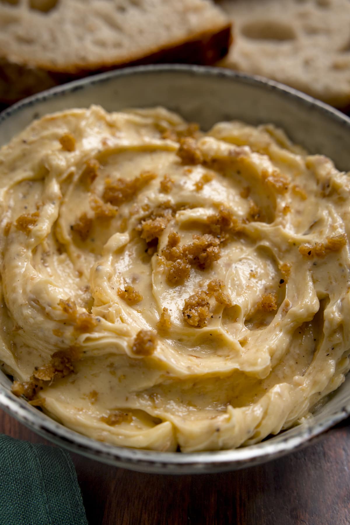 Tall close up image of chicken skin butter in a bowl. There are slices of bread in the background.