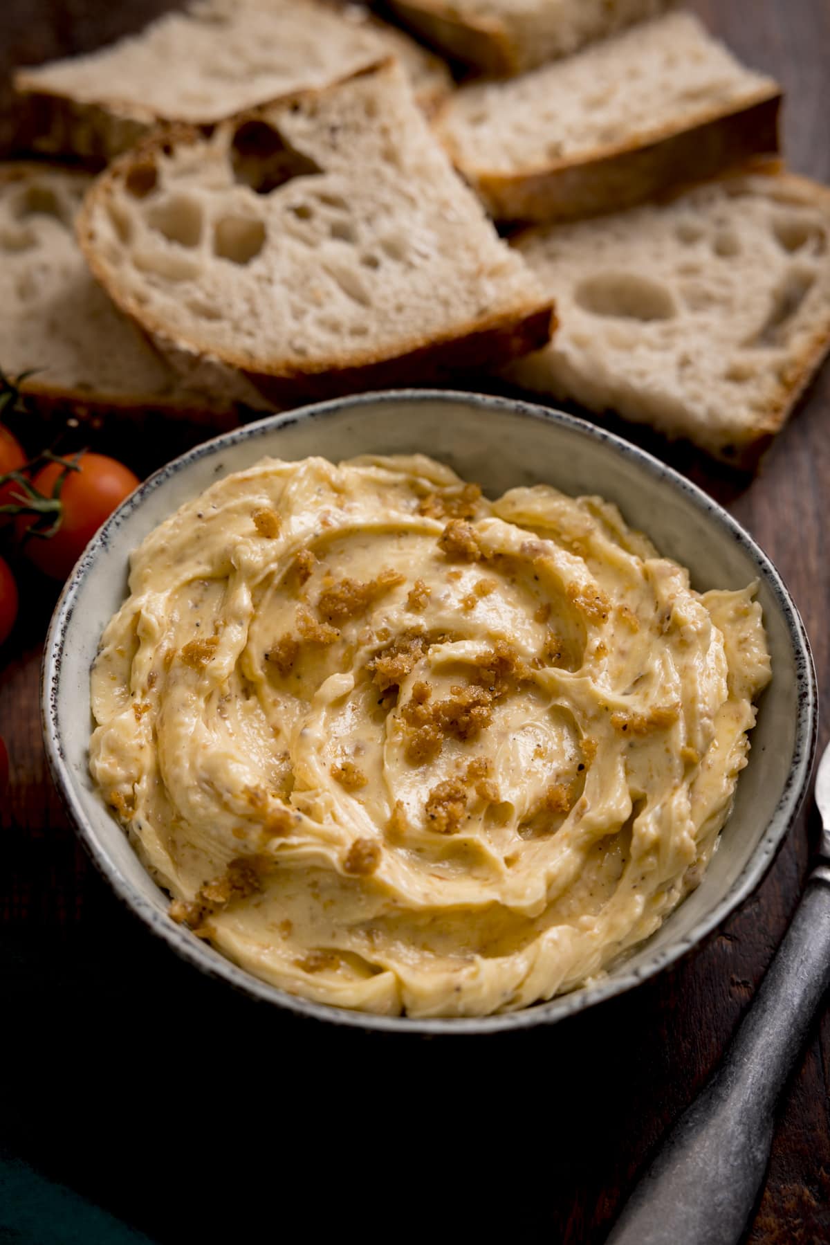 Close up of a bowl of chicken skin butter with slices of bread in the background.