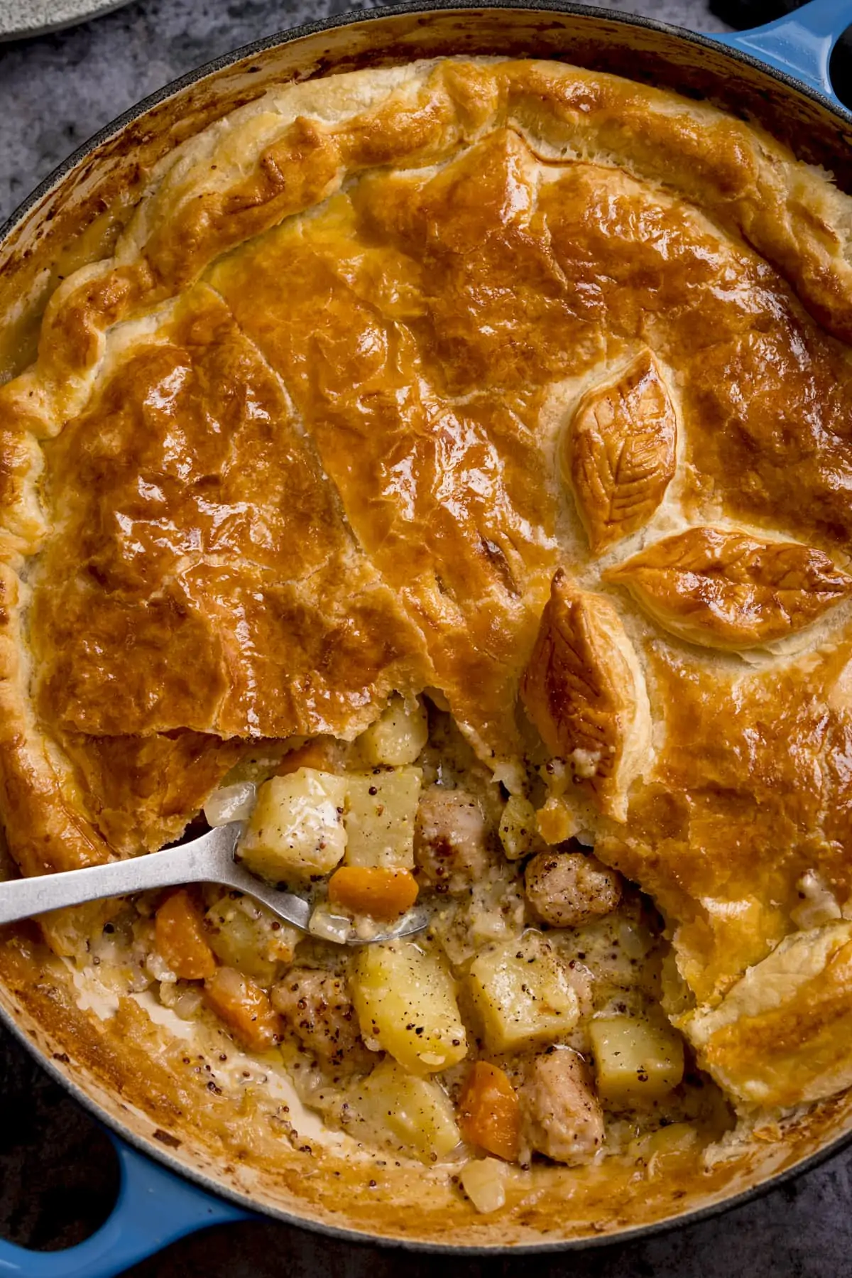 Tall overhead image of a sausage and mustard pie with some of the pastry lid removed. There is a spoonful being taken from the pie.