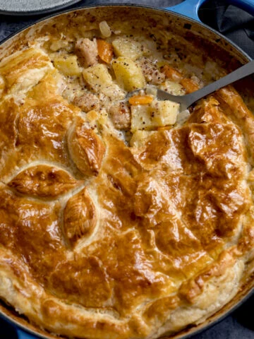 Square image of a sausage and mustard pie - shot from overhead. There is a spoonful of the pie filling being taken out.
