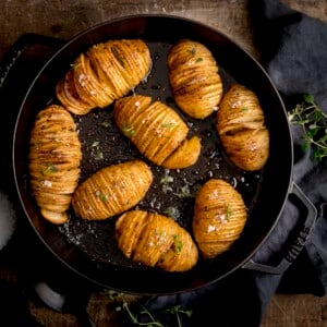 Hasselback potatoes in a black cast iron pan on a wooden table next to a dark grey napkin.