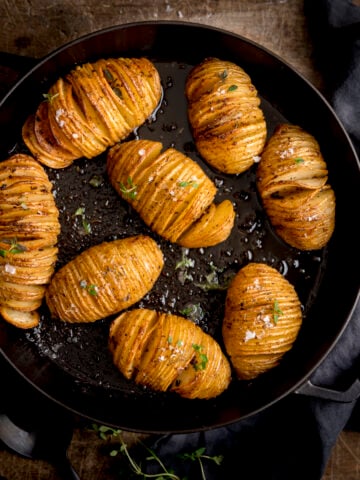 Hasselback potatoes in a black cast iron pan on a wooden table next to a dark grey napkin.