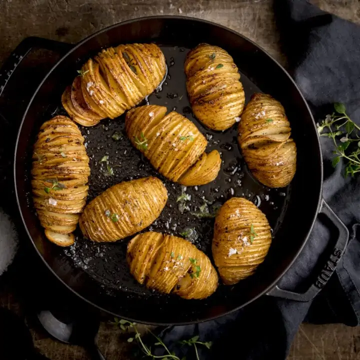 Hasselback potatoes in a black cast iron pan on a wooden table next to a dark grey napkin.
