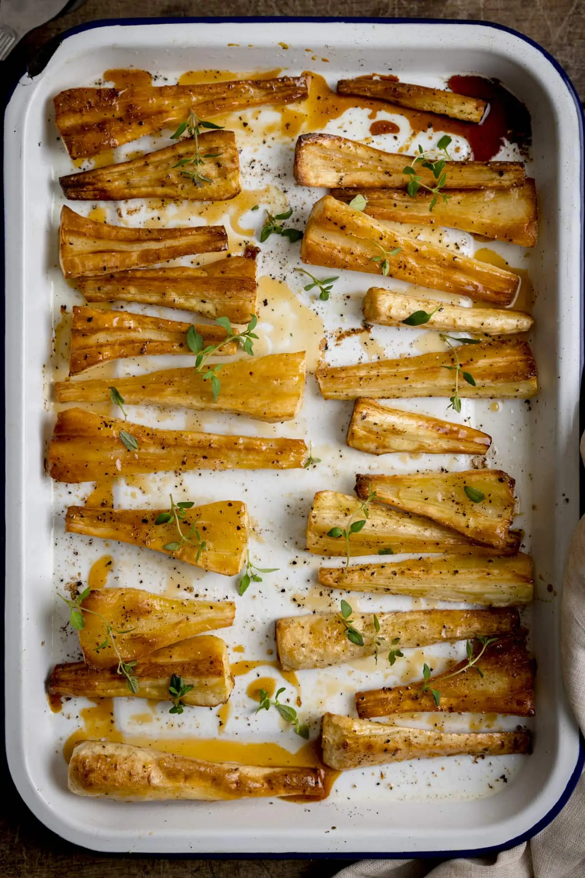 Honey roasted parsnips laid out on a white baking tray and sprinkled with fresh thyme