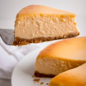 A closeup of a square image of a slice taken from a New York Cheesecake against a white background.
