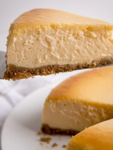 A close up square image of a slice being take from a New York Cheesecake against a white background.