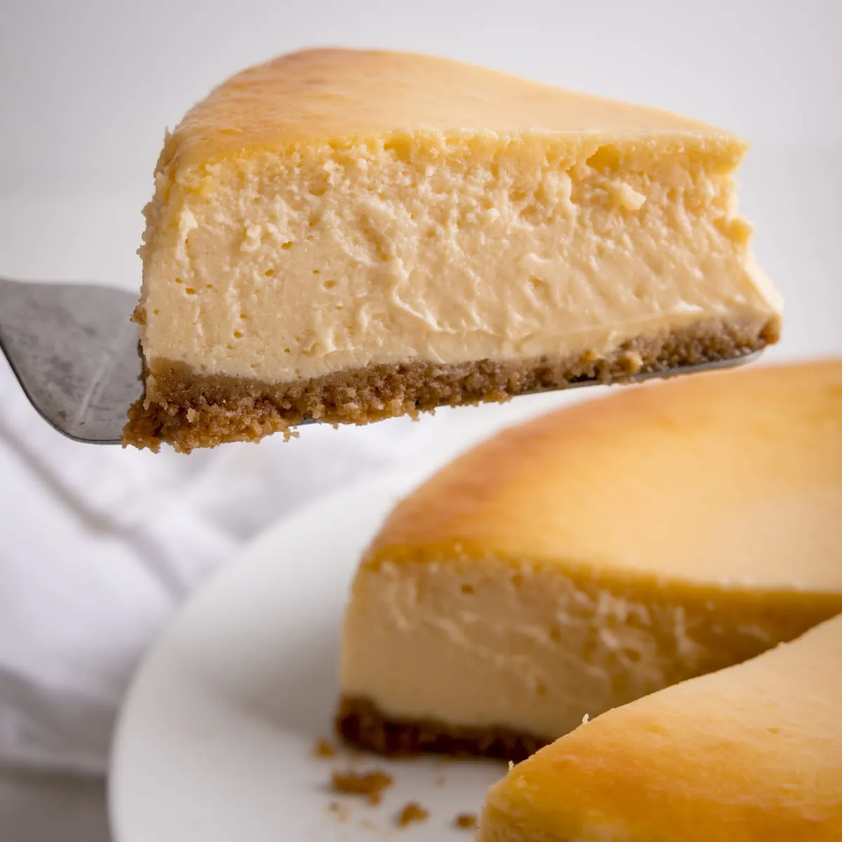 A close up square image of a slice being take from a New York Cheesecake against a white background.