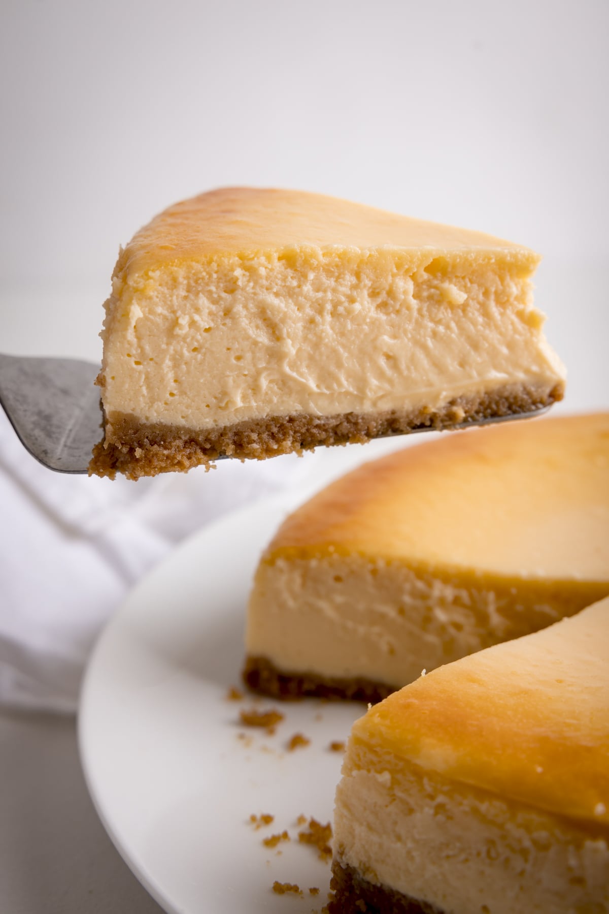 A close up of a slice being take from a New York Cheesecake against a white background.
