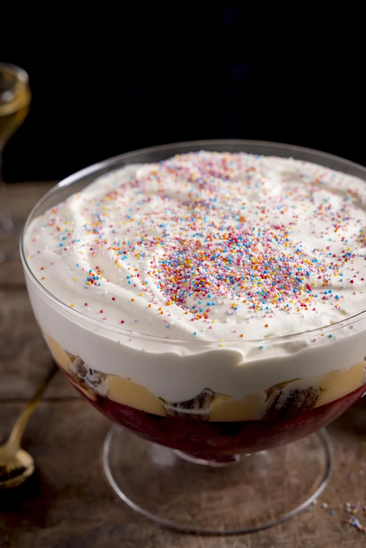 Sherry trifle, topped with sprinkles, on a wooden table.