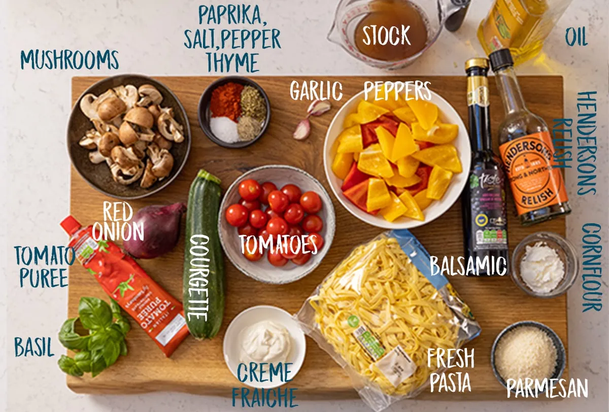 Ingredients for roasted vegetable pasta on a wooden board on a white background.