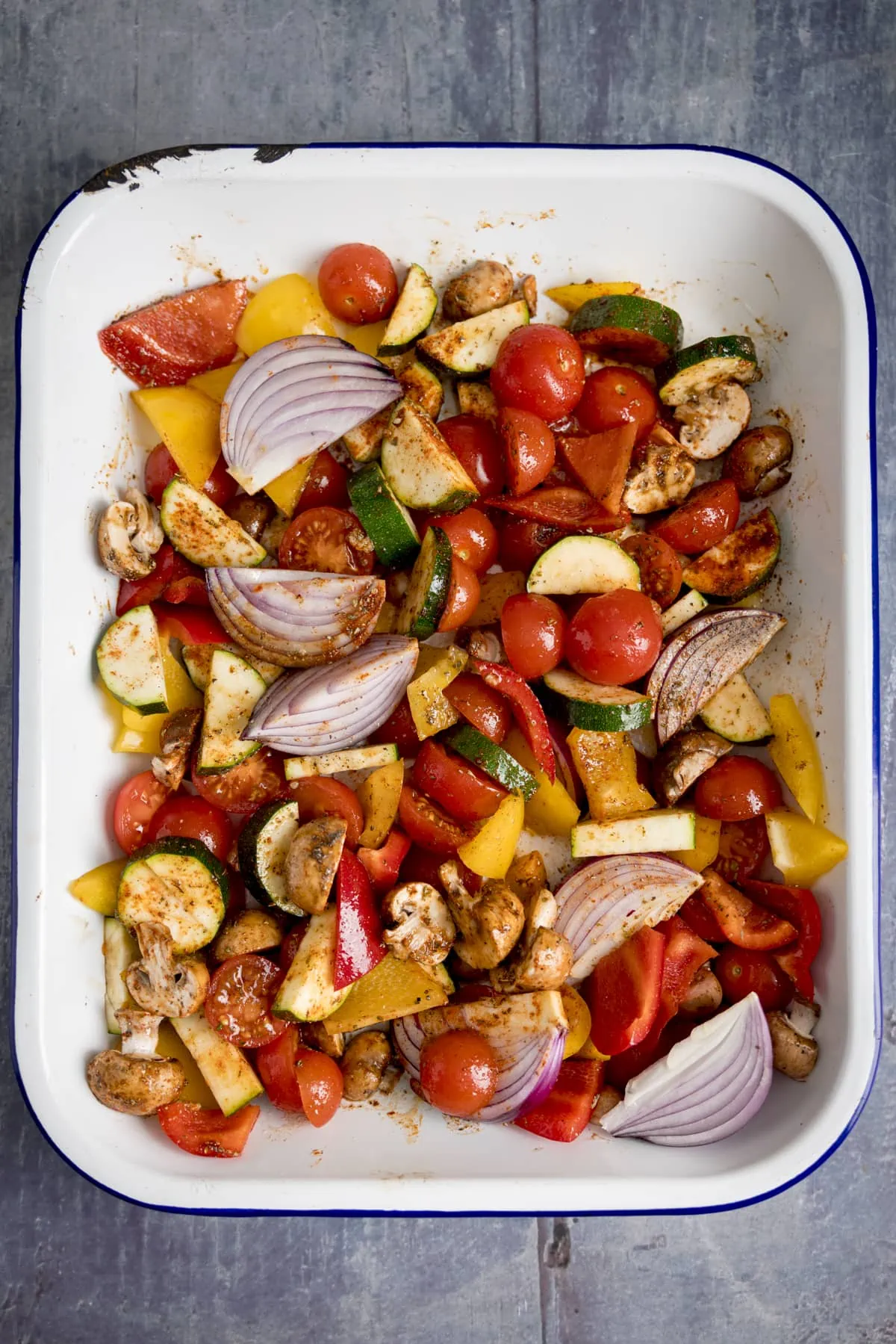 Overheard of a white tray filling with chopped vegetables on a blue background.