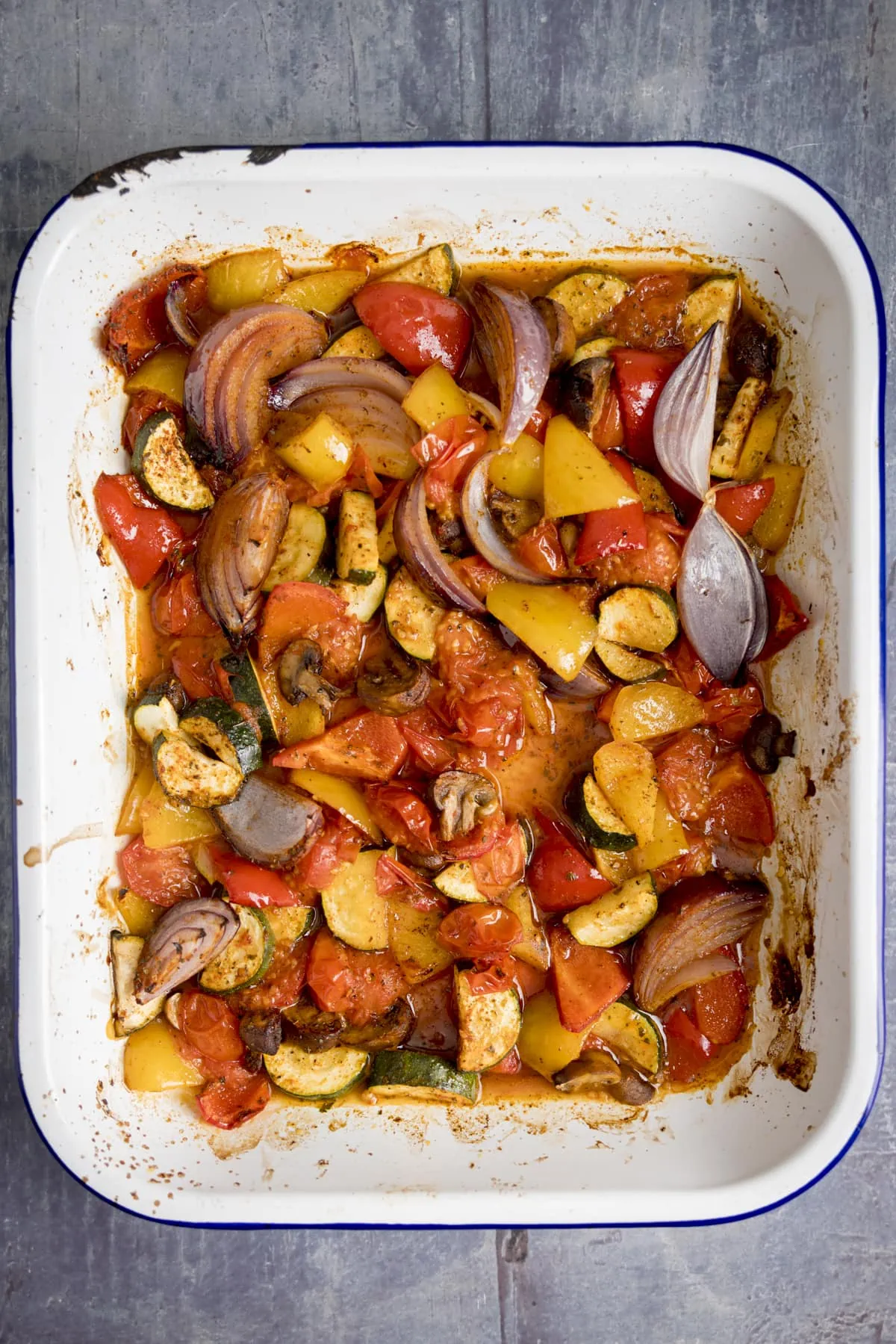 Overheard of a white tray filling with chopped roasted vegetables on a blue background.