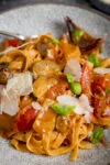 Close up of a Bowl of roasted vegetable tagliatelle topped with basil leaves and shaved cheese.