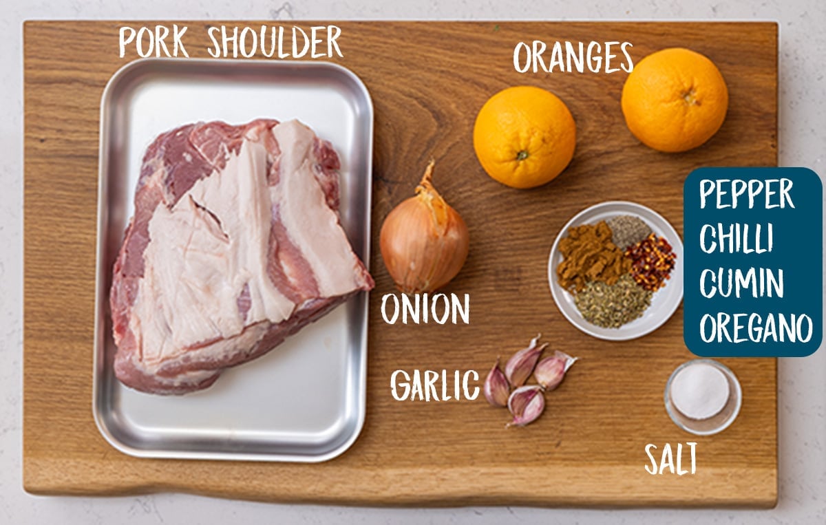 Ingredients for pork carnitas on a wooden board.