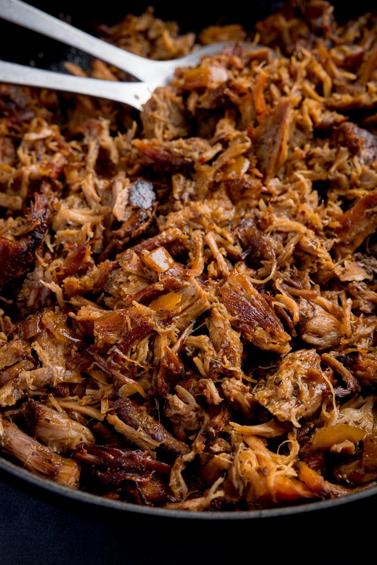 Close up image of pork carnitas frying in a pan.