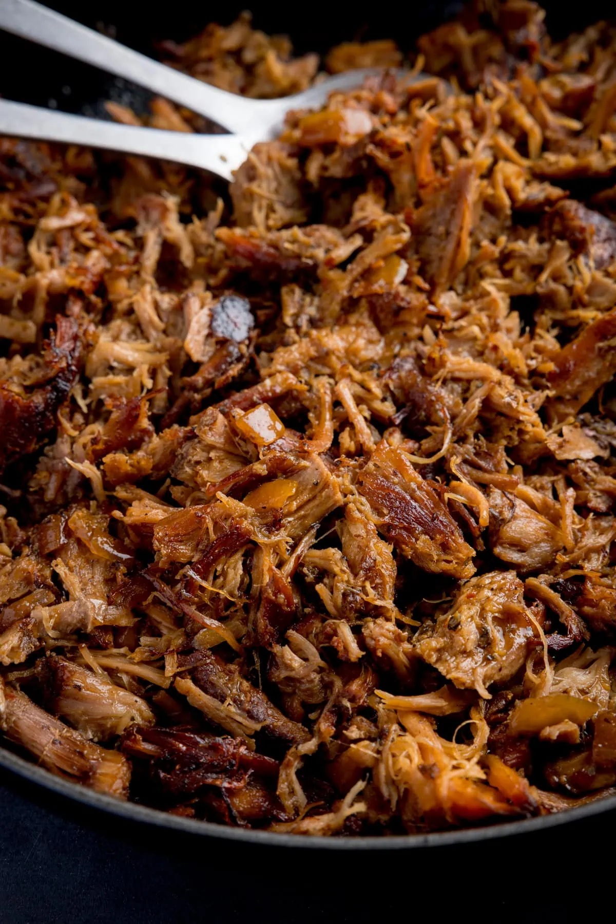 Close up image of pork carnitas frying in a pan.