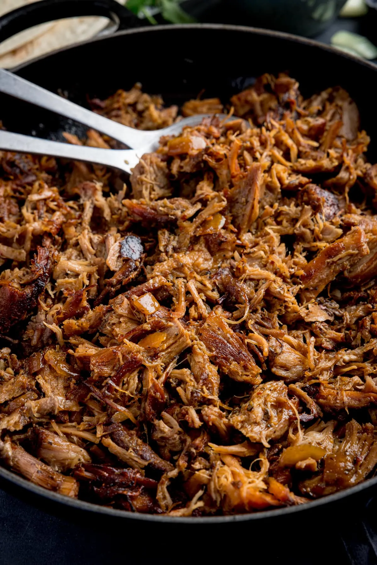 Tall image of a frying pan filled with pork carnitas.