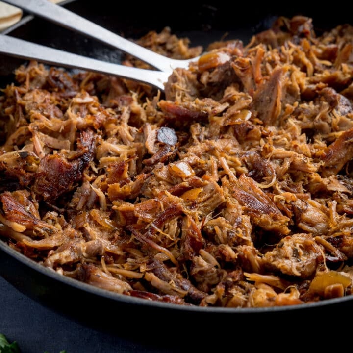 Square image of a pan of pork carnitas being fried.