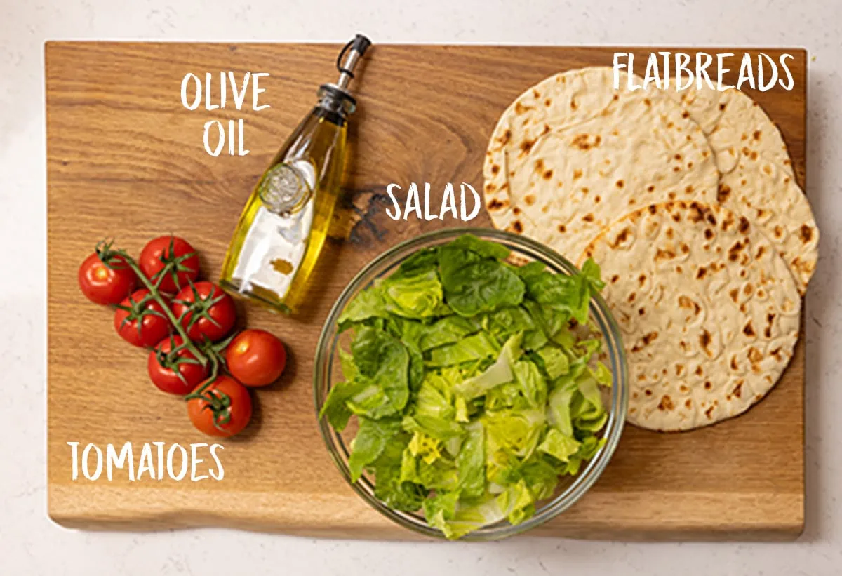 flatbreads, olive oil, tomatoes and chopped lettuce on a wooden board.