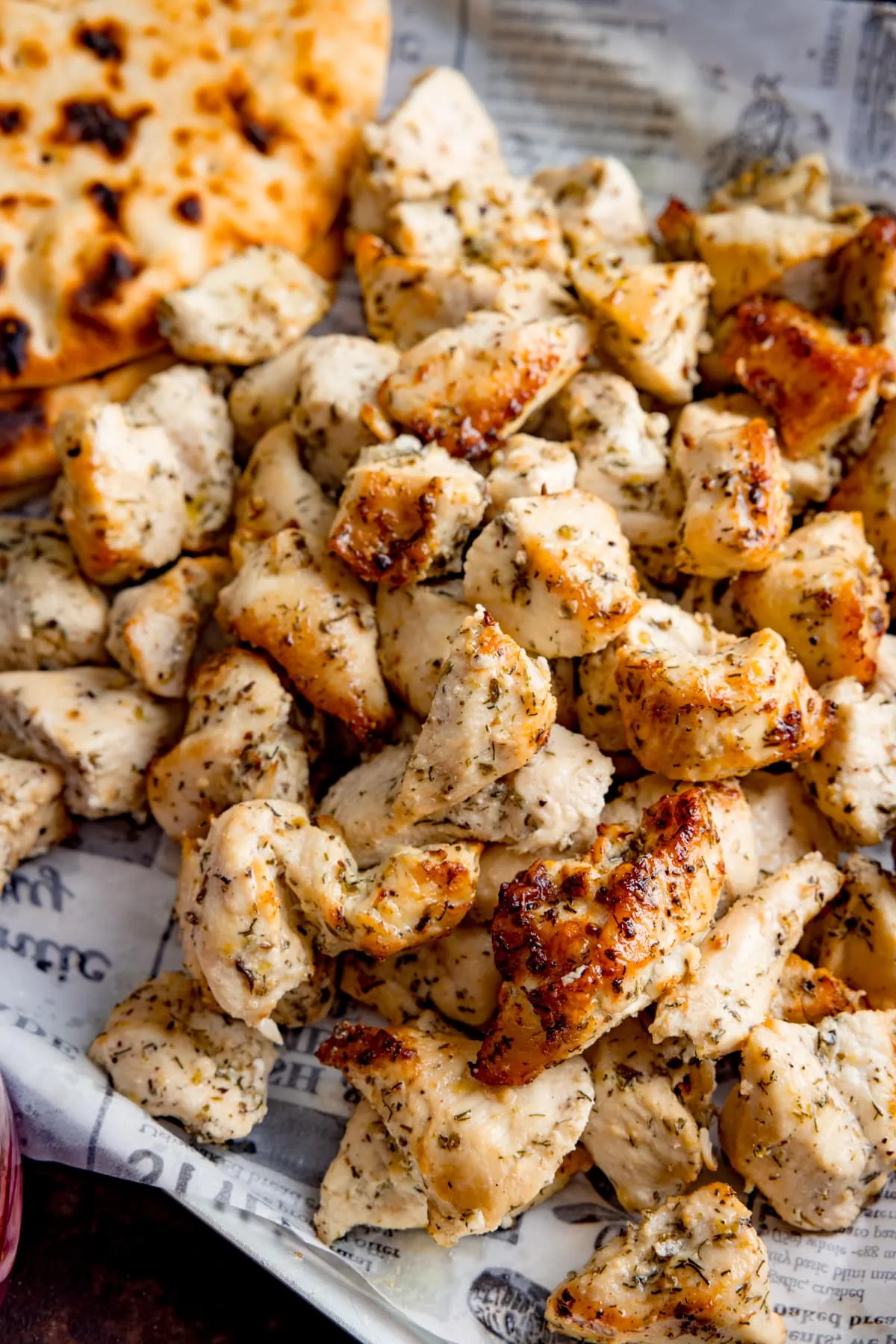 Close up image of air fried Greek marinated chicken pieces on a tray line with paper, next to some flatbreads.