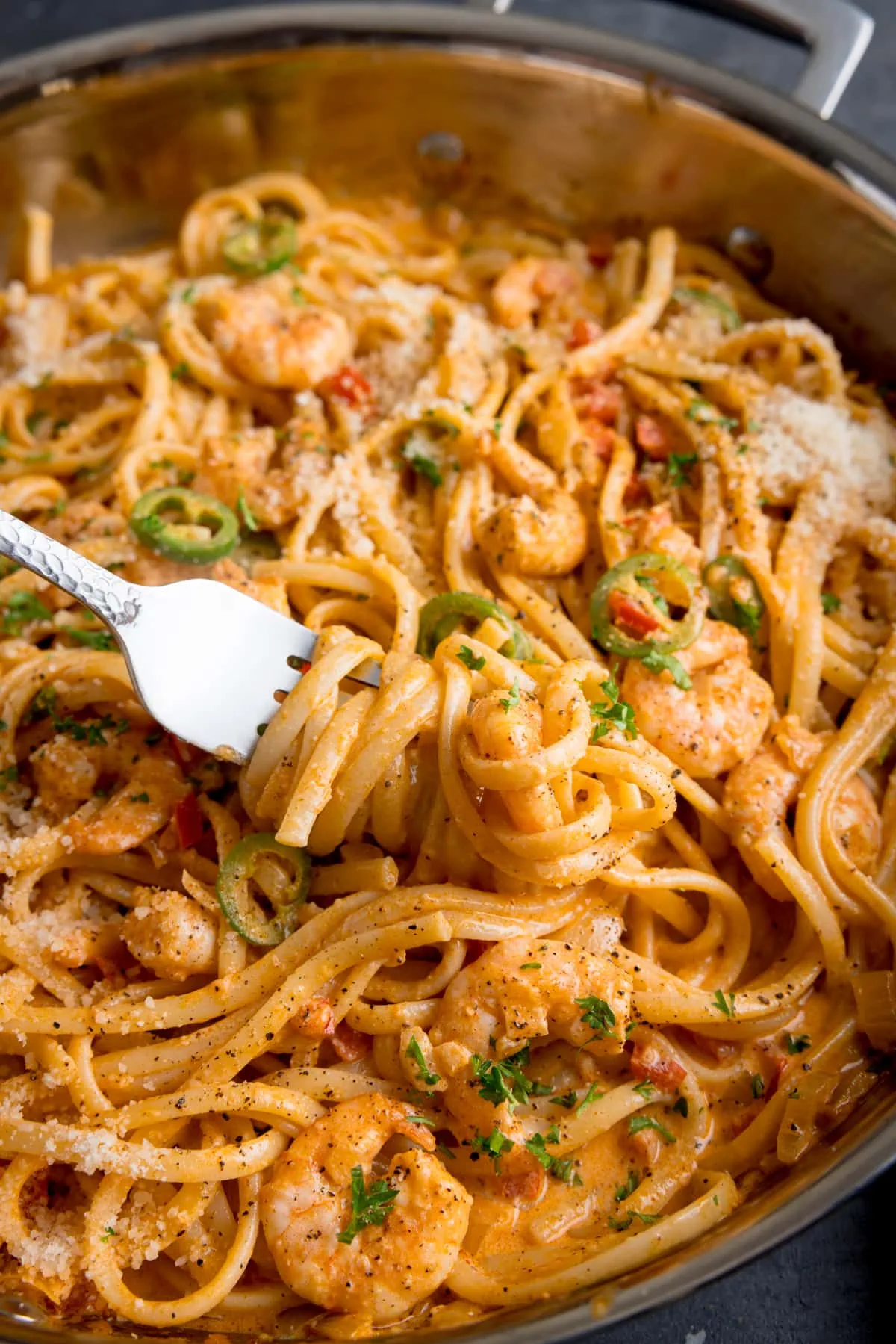 Tall image of a pan of prawn linguine in a creamy buffalo sauce. There is a fork taking some of the pasta from the pan.