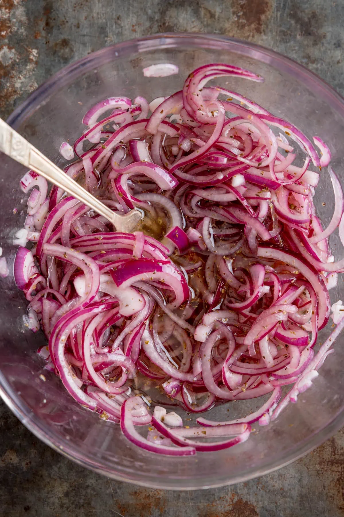 Picture above: marinated red onion slices in a glass bowl with a metal spoon sticking out.