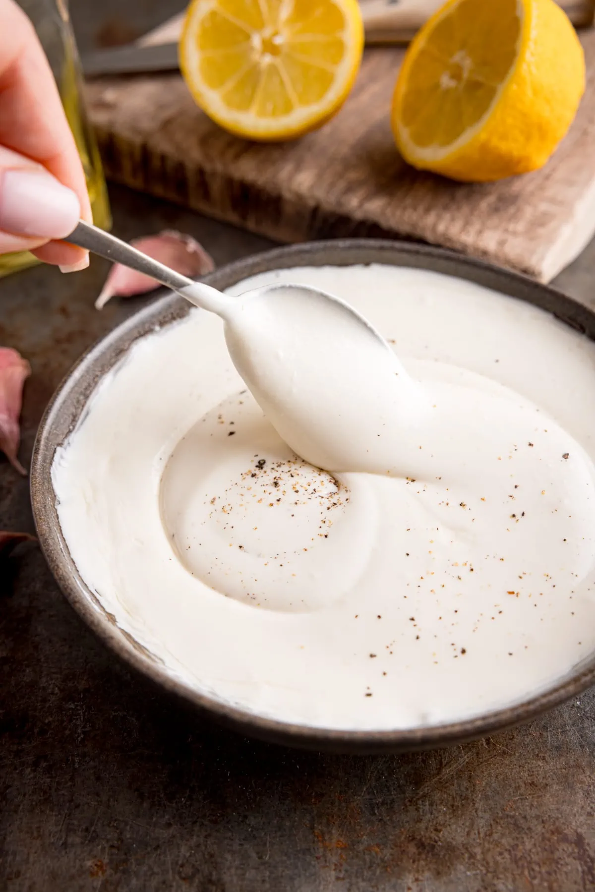 Whipped feta in a dark bowl being stirred. A lemon, chopped in half is in the background.