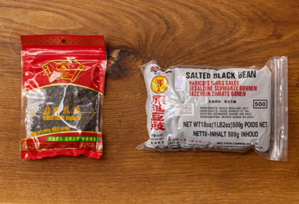 Two different packets of fermented black beans on a wooden board.