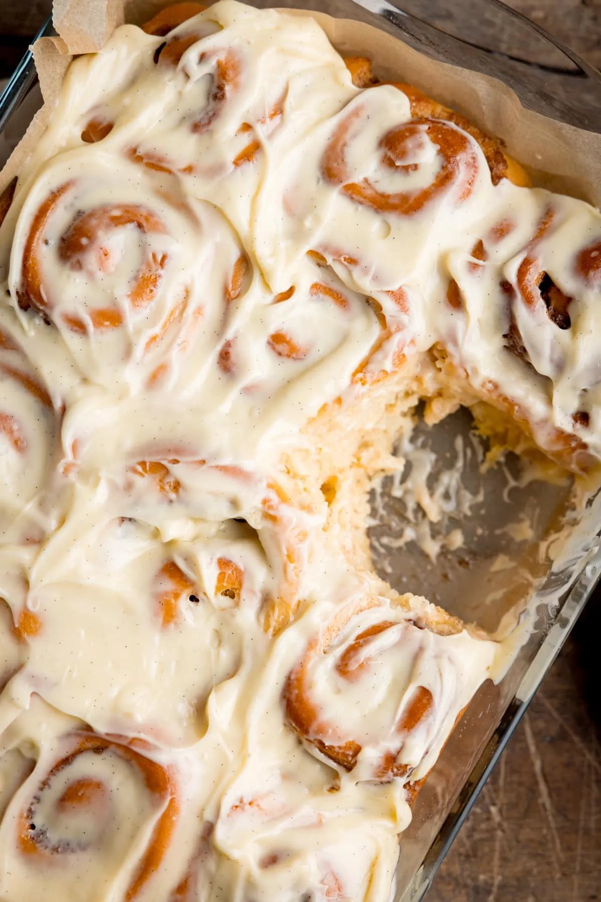 Overhead image of a baking dish filled with cinnamon rolls, topped with cream cheese frosting. One cinnamon roll has been removed.