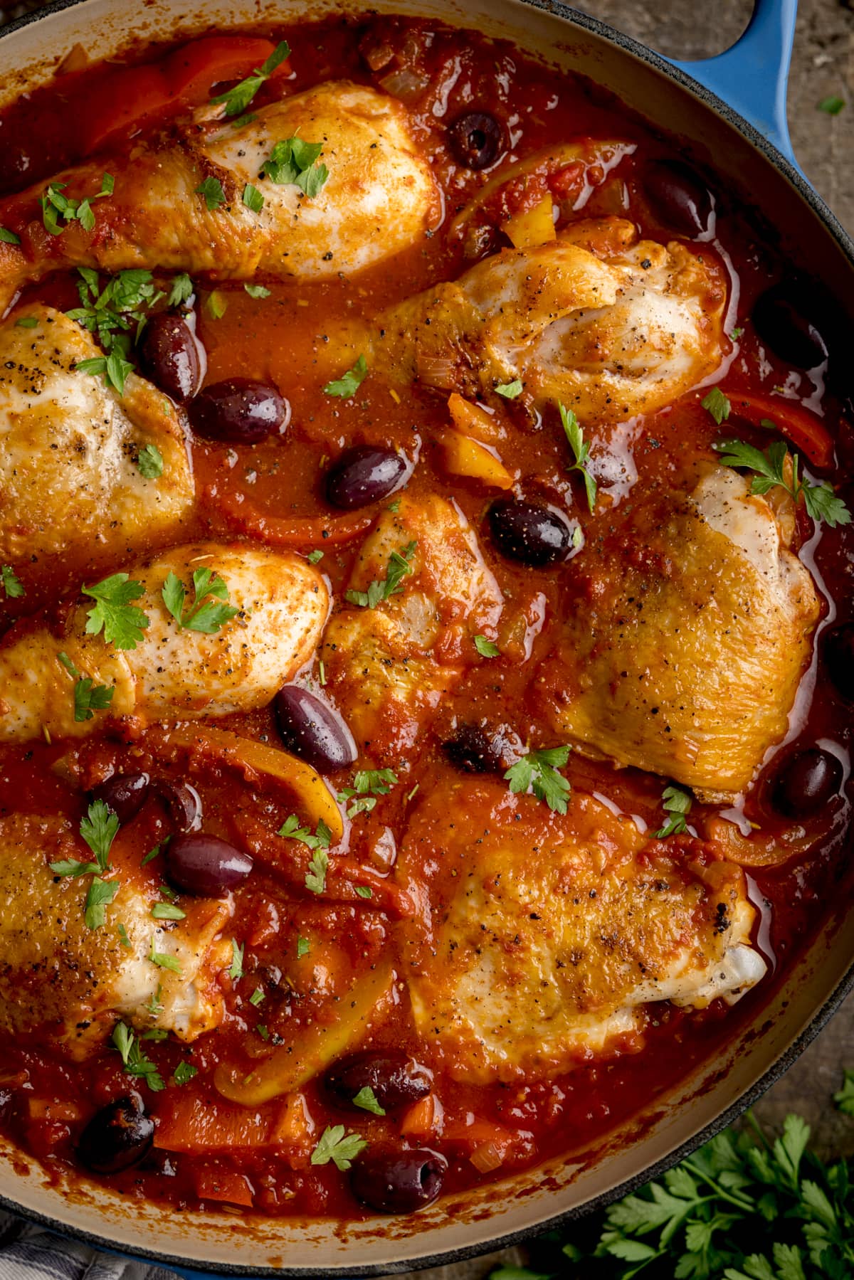Close-up overhead image of chicken cacciatore in a large, shallow blue casserole dish.
