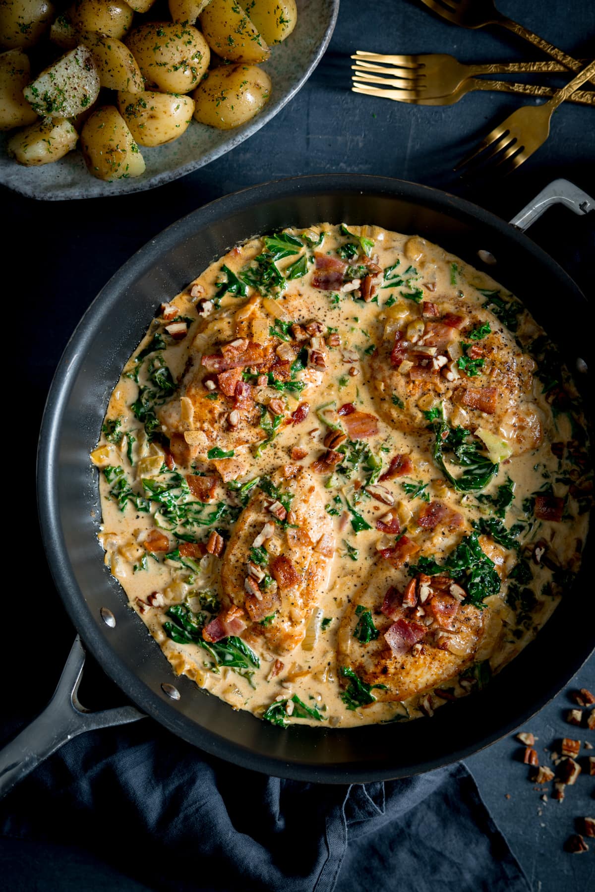 Overhead picture of creamy chicken dijon in a frying pan that is sat on a grey/blue board with gold forks in the top right corner.