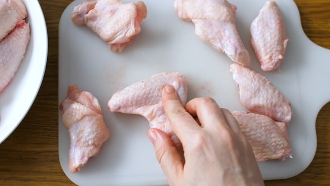 Chicken wings about to be cut into two pieces on a white chopping board