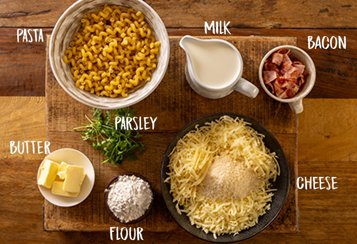 Individually labelled ingredients for a four cheese mac n cheese on a wooden board.