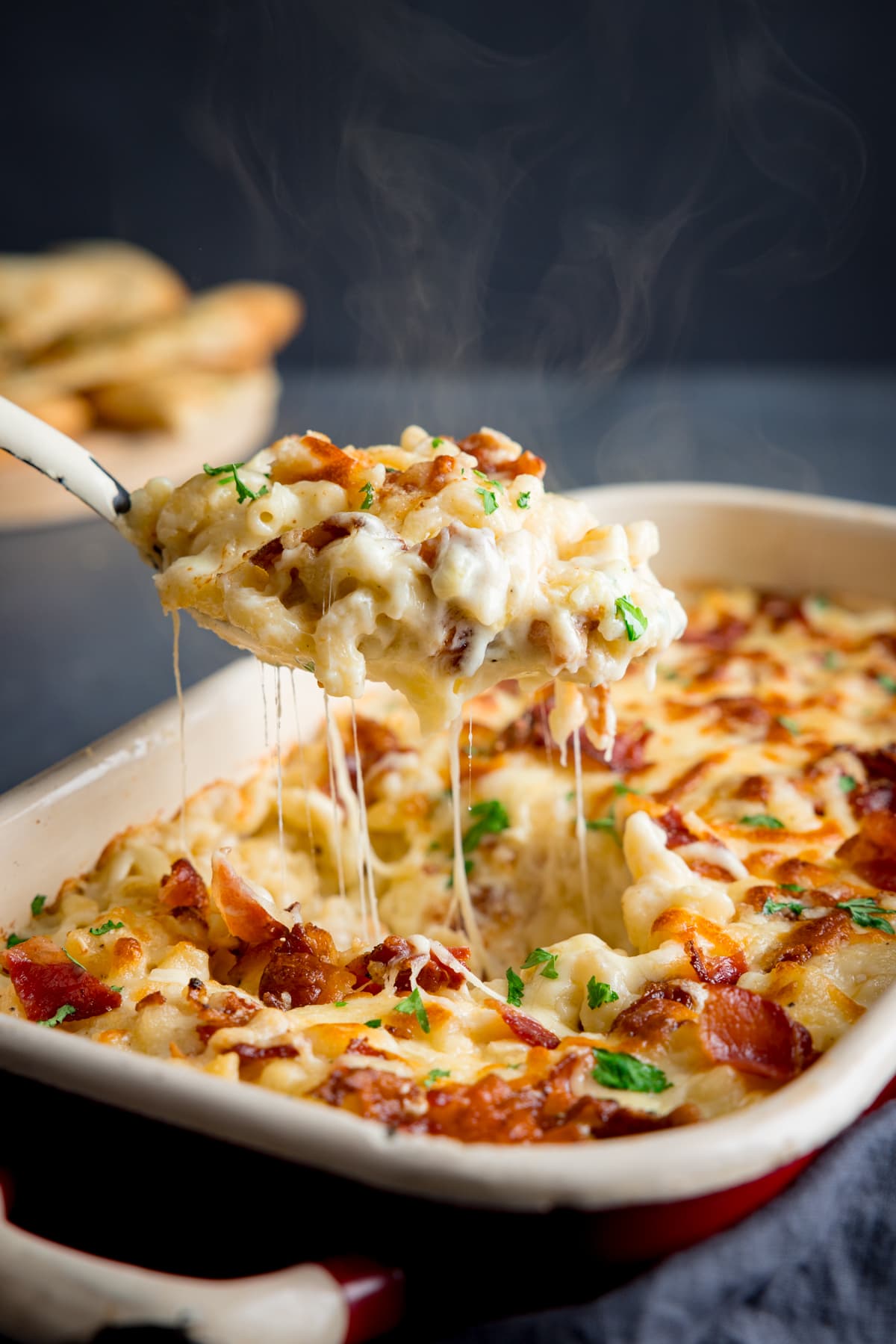 Close up picture of some steamy cheesy mac n cheese been spooned out of a baking dish full of four cheese mac n cheese.